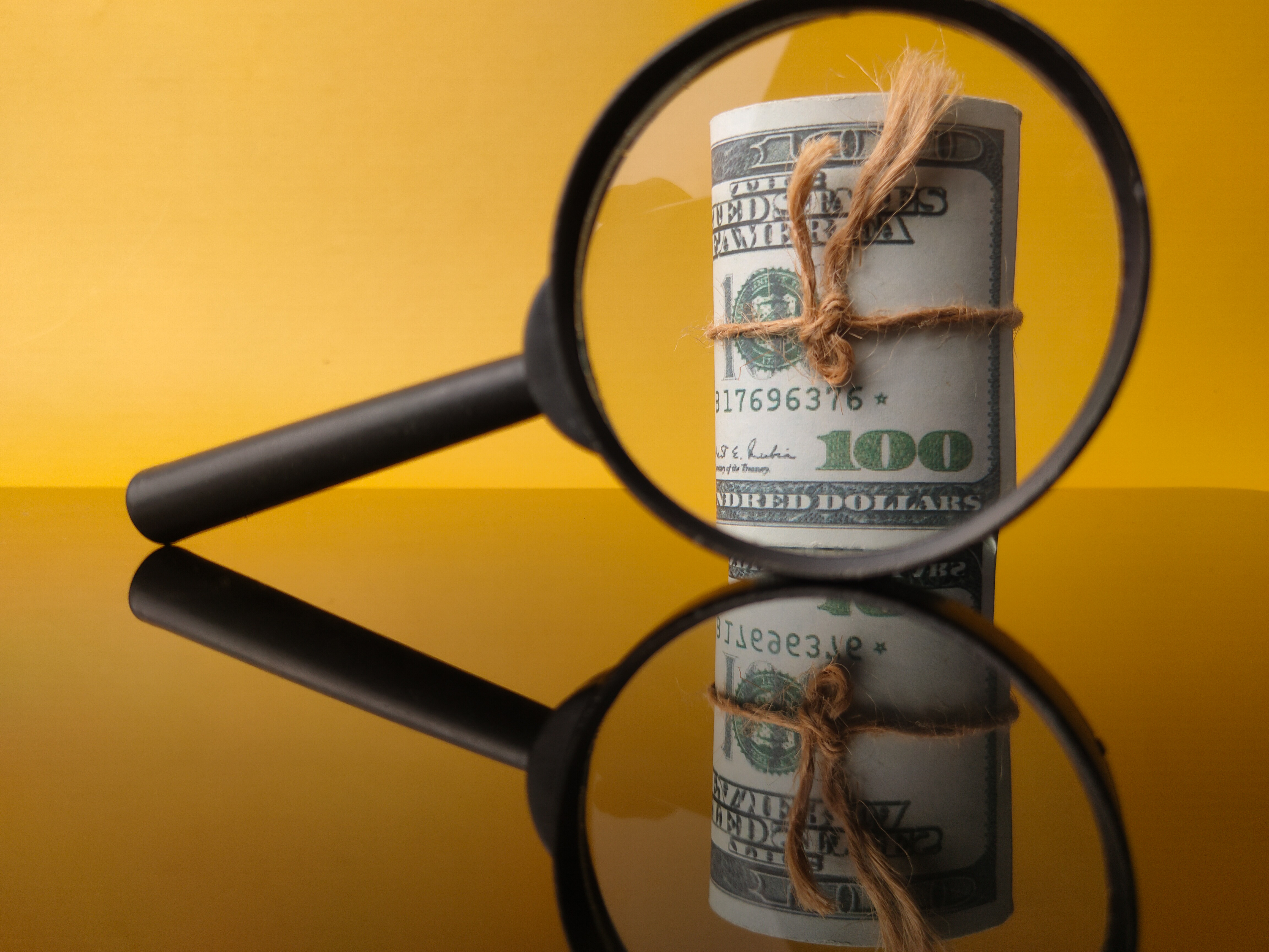 Hidden Costs: banknotes-magnifying-glass-with-reflection-yellow-background